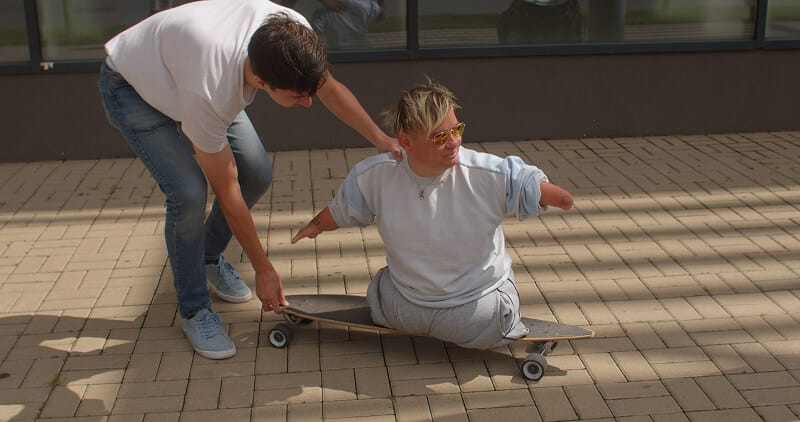 Photo of a man with no legs riding on a skateboard with assistance