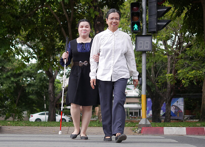Photo of a vision impaired person being assisted by another person on a road crossing