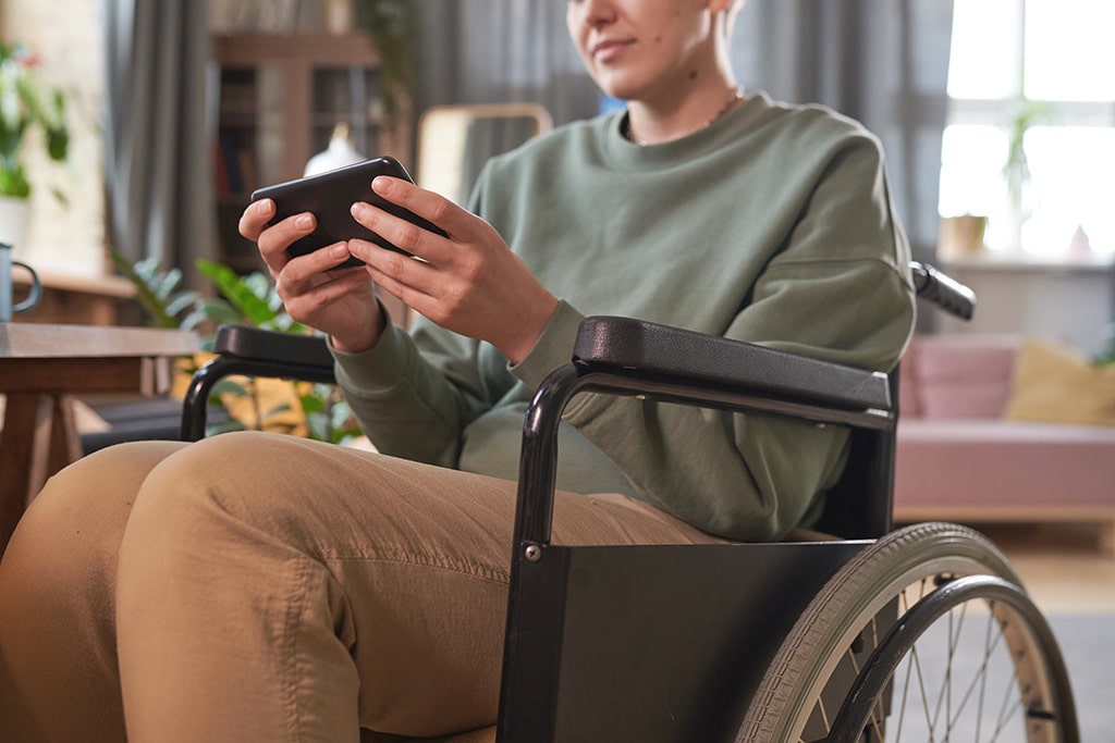 Close-up of a person sitting on wheelchair and typing on mobile phone talking online during her leisure time