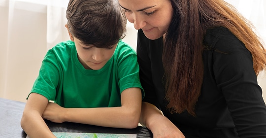 A lady helping a boy. They are both working on a tablet device together.