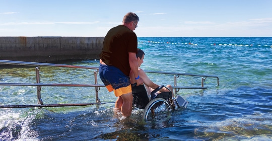 Photo of a person being assisted into shallow water at the beach