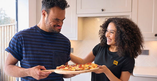 Two people smiling. They have made pizza.