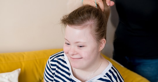 A person helping tie a girl's hair in a ponytail