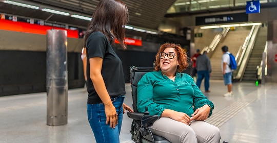 Photo of a person in a wheelchair on a train platform talking to another person