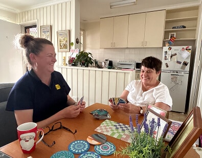 Photo of a support worker and a client sitting at a table playing Uno