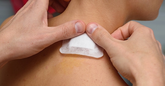 A person applying a band-aid to the back of someone's neck