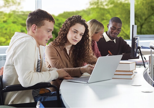 Two students in a classroom looking at a laptop