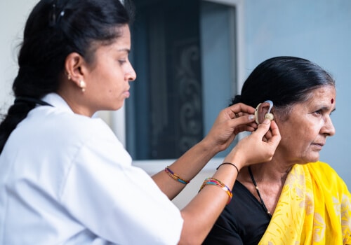 A younger woman assists an older woman in fitting a hearing aid
