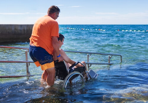 A man helping wheel a man in a wheelchair into the ocean via an assistive ramp