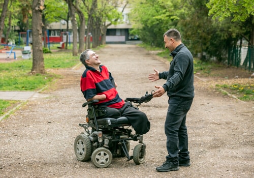 Two men laughing together. One man is in a wheelchair while the other is standing and gesturing with arms open