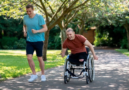Two friends competing. One of them is running while the other is in a wheelchair alongside.