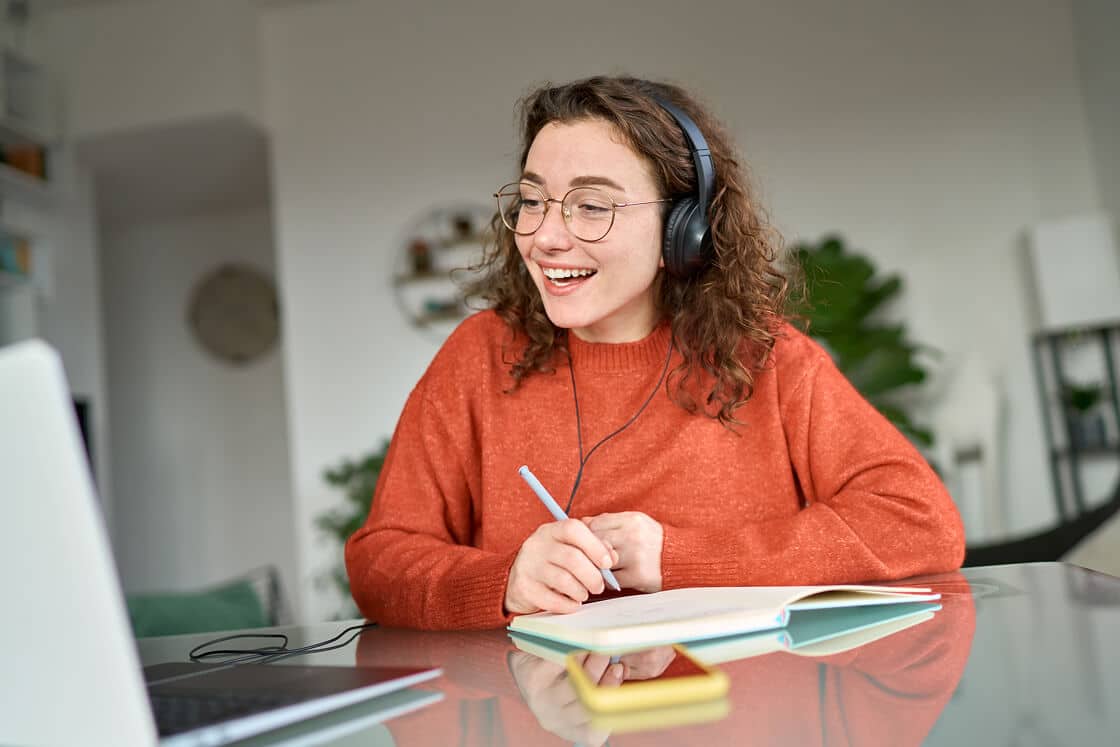 A woman with a headset on, smiling and taking notes on a notepad
