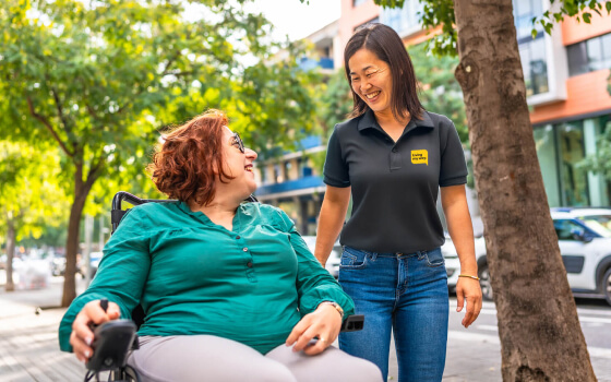 A woman in a wheelchair smiling at her support worker