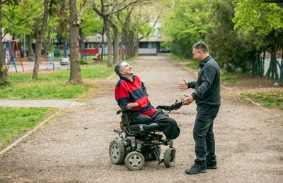 A man in a wheelchair laughing with a man standing in front of him with his arms open, smiling