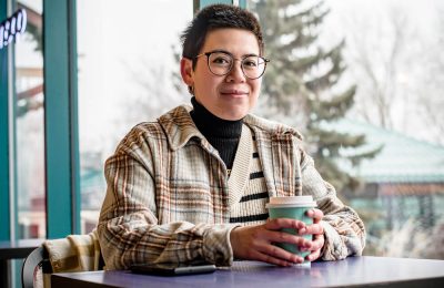 A woman sitting at a table with a takeaway cup of coffee, smiling