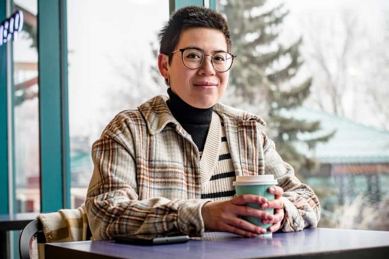 A woman sitting at a table with a takeaway cup of coffee, smiling