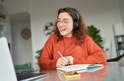 A woman with a headset on, smiling and taking notes on a notepad